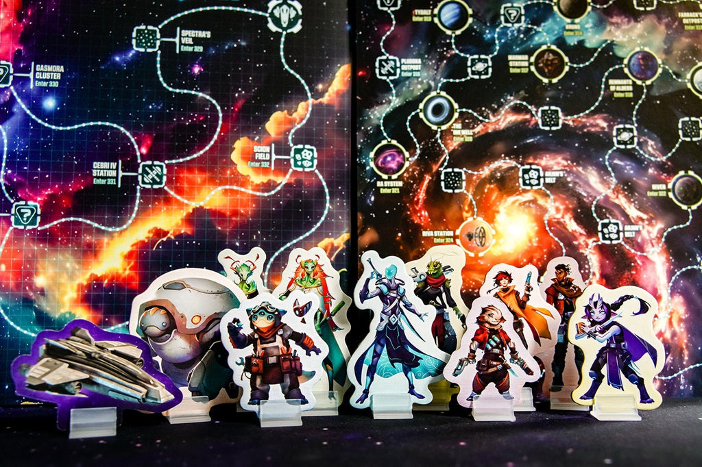 Colorful cardboard character standees and a spaceship are set before the vibrant Wandering Galaxy: A Crossroads Game map by Plaid Hat Games, displaying planets, stars, and connecting pathways in the background.