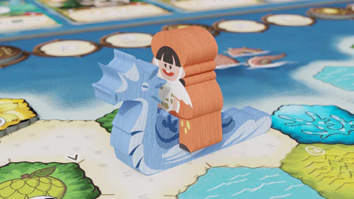 A wooden game piece shaped like a smiling girl riding a blue dragon figurine from Bad Comet's Wondrous Creatures is placed on the vibrant game board filled with water, land, and tokens.