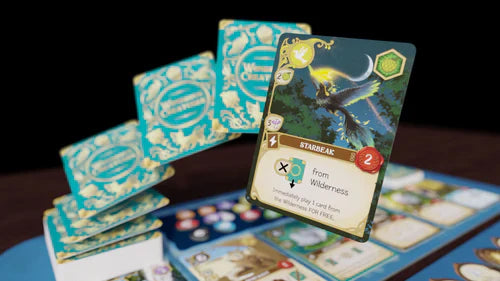 A close-up of Wondrous Creatures by Bad Comet shows a fantasy tableau-building card game setup, highlighting a winged creature under the moon card, with stacks of decorative square cards arranged on the game board.