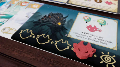 A close-up of Bad Comet’s Wondrous Creatures: Gargantuan Beasts Expansion shows a card with a dark beast, tokens, and a red dragon-shaped piece on the beast tracker, all arranged on a wooden table.