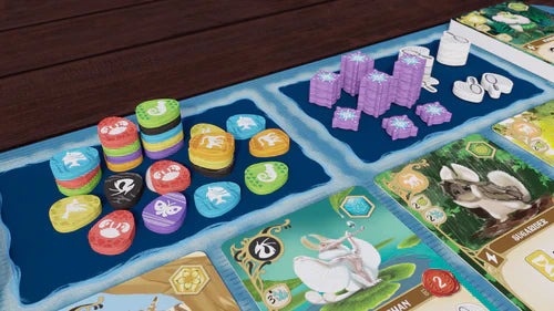 A close-up shows the Wondrous Creatures: Upgraded Components Expansion by Bad Comet, featuring colorful stacked tokens, purple hex tokens, white round tokens, wooden upgrades, and illustrated cards on a blue and wood surface.