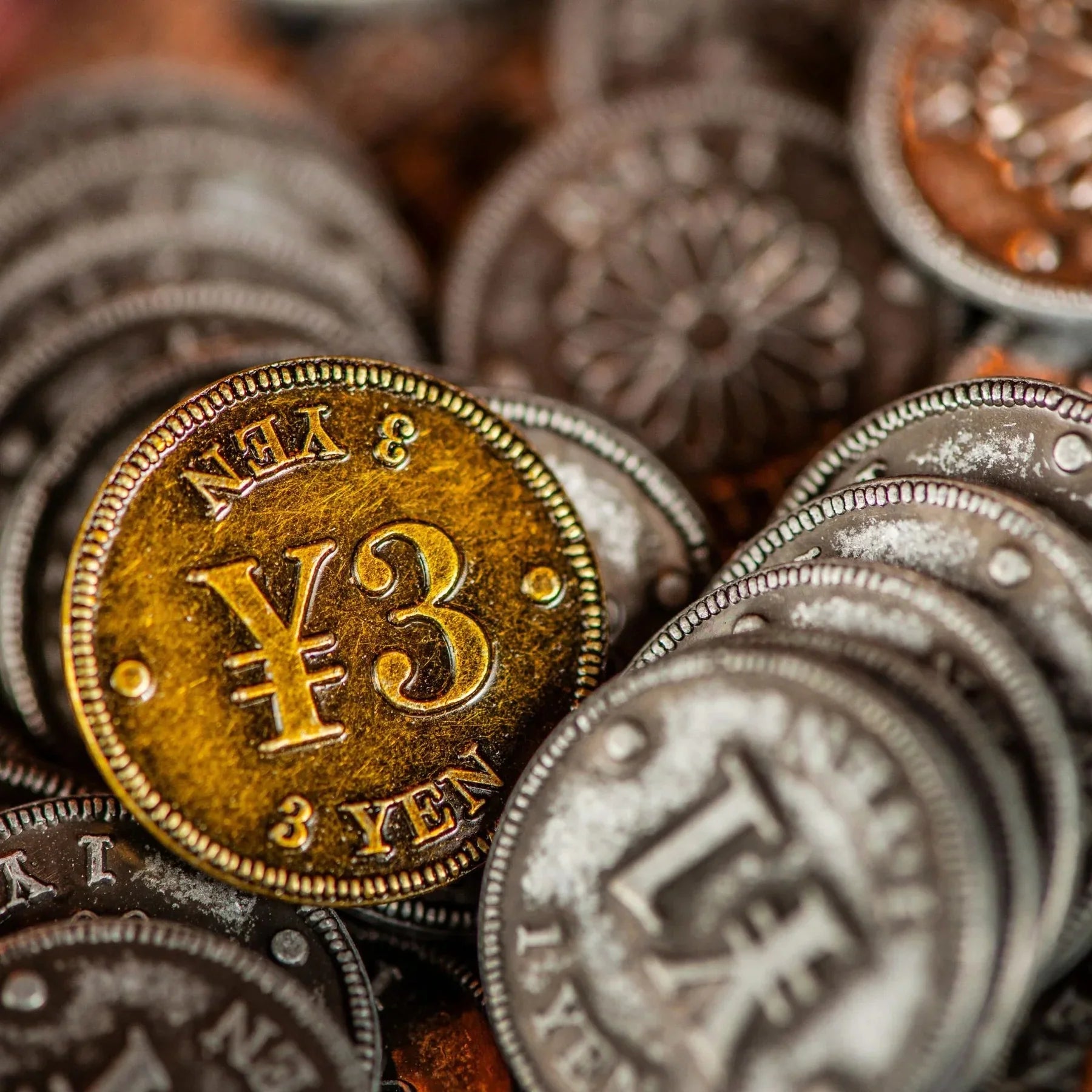 A close-up of Yokohama: Premium Tokens by Synapses Games shows a shiny gold 3 yen coin among silver coins—ideal as unique board game accessories or as premium tokens for your next game night.