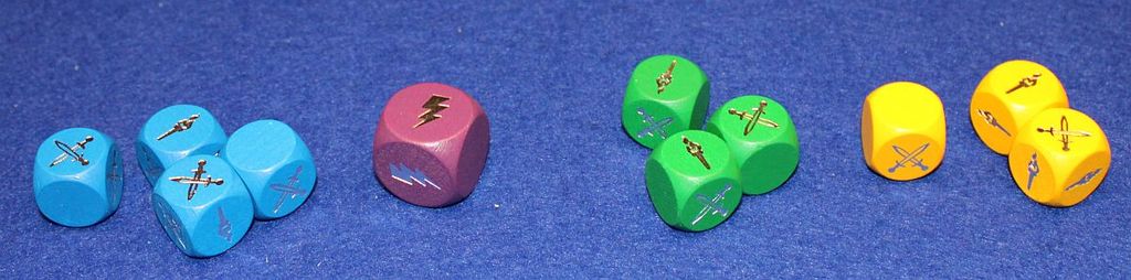 Five sets of colorful dice—three blue, one purple, three green, and three yellow—featuring swords and lightning bolts are arranged on blue felt. These dice are essential for Kosmos’s Andor: The Family Fantasy Game.