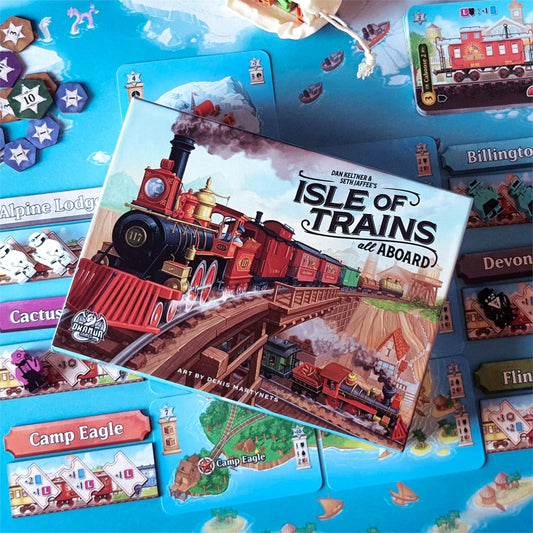 The Isle of Trains: All Aboard Deluxe Edition is shown with a red steam engine on its box, surrounded by illustrated map tiles and tokens in this vibrant engine-building board game setup.