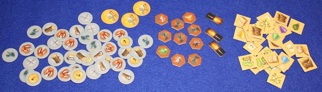 Game tokens for Kosmos’ Andor: The Family Fantasy Game are arranged on a blue surface: circular tokens with icons on the left, orange hexagonal and black rectangular tokens in the center, and yellow square tokens with symbols on the right.