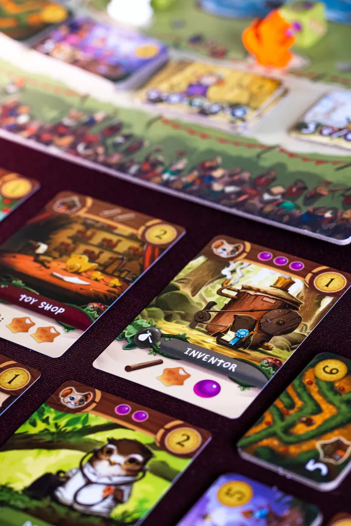 Close-up of colorful My Lil' Everdell cards from Starling Games (II) on a table, including Toy Shop and Inventor, with whimsical animal characters—a charming worker-placement game designed for kids.